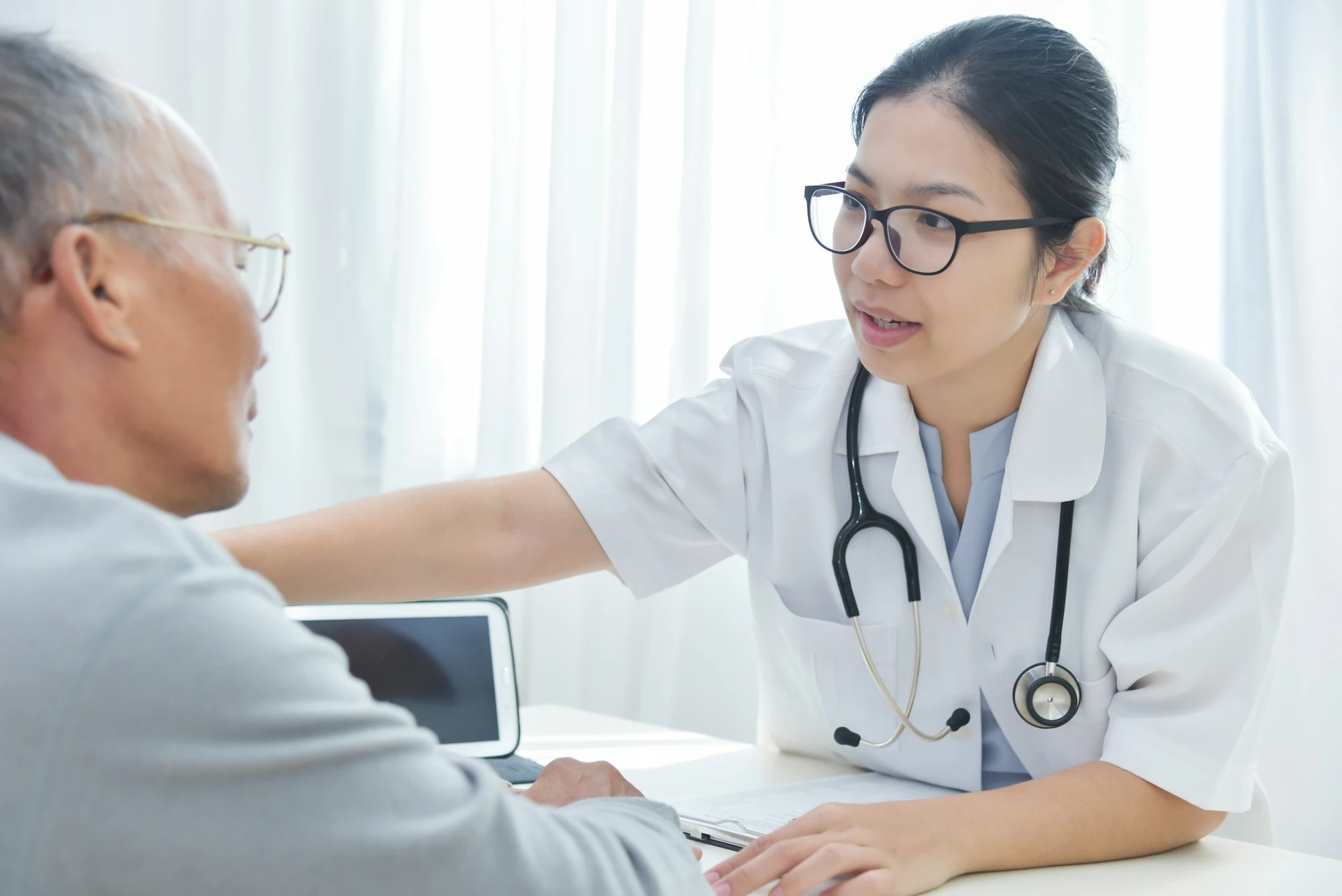 A female doctor with a stethoscope speaking compassionately to an elderly patient.